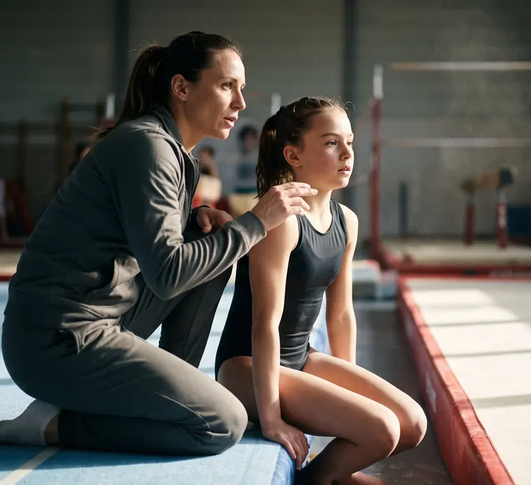 Une entraîneure parle à une jeune gymnaste assise au bord du praticable